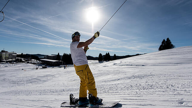 Ein Snowboarder fährt auf dem Feldberg im Schwarzwald mit dem Skilift.