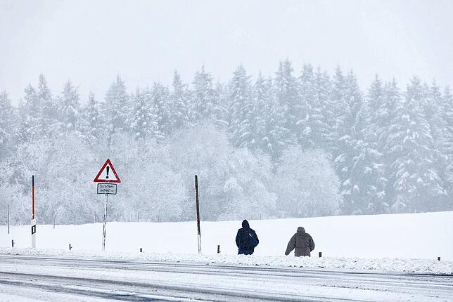 Menschen gehen in Oberried auf dem Schauinsland neben einer Straße durch den Schnee.